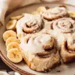 Delicious banana bread cinnamon rolls drizzled with icing on a wooden table.