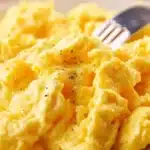 Plate of cheesy scrambled eggs garnished with herbs