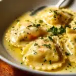 Plate of Lobster Ravioli topped with Lemon Butter Sauce and garnished with herbs