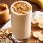 Healthy peanut butter oatmeal smoothie in a glass with oats and bananas