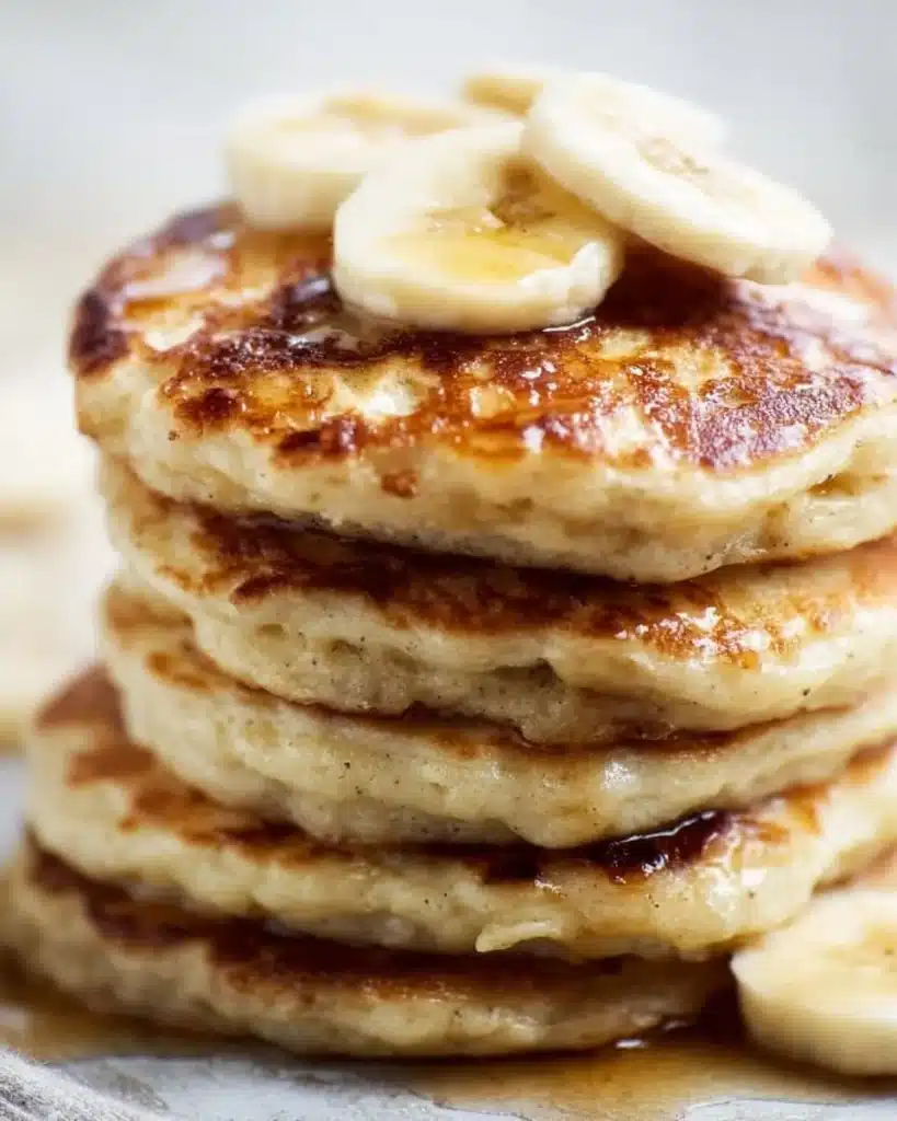 Fluffy vegan banana pancakes stacked on a plate with syrup and fruit