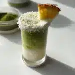 Pineapple Coconut Milk Matcha Latte in a glass with tropical decorations